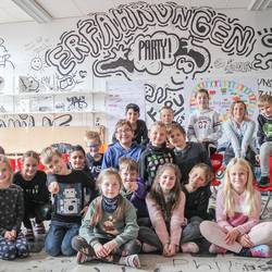 Schülerinnen und Schüler der Grundschule Ingeln-Oesselse präsentieren in einem schwarzweiß bemalten Raum die Ergebnisse des Projektes miteinanderfüreinander..